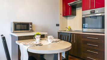 A kitchen with a microwave, oven, and red cabinets. There is a table with a floral tablecloth, a flower vase, and a coffee pot.