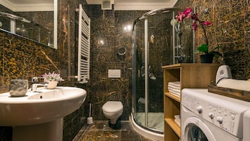 Um banheiro moderno com painel de fundo de mármore, chuveiro com box de vidro, máquina de lavar embutida e vaso sanitário.