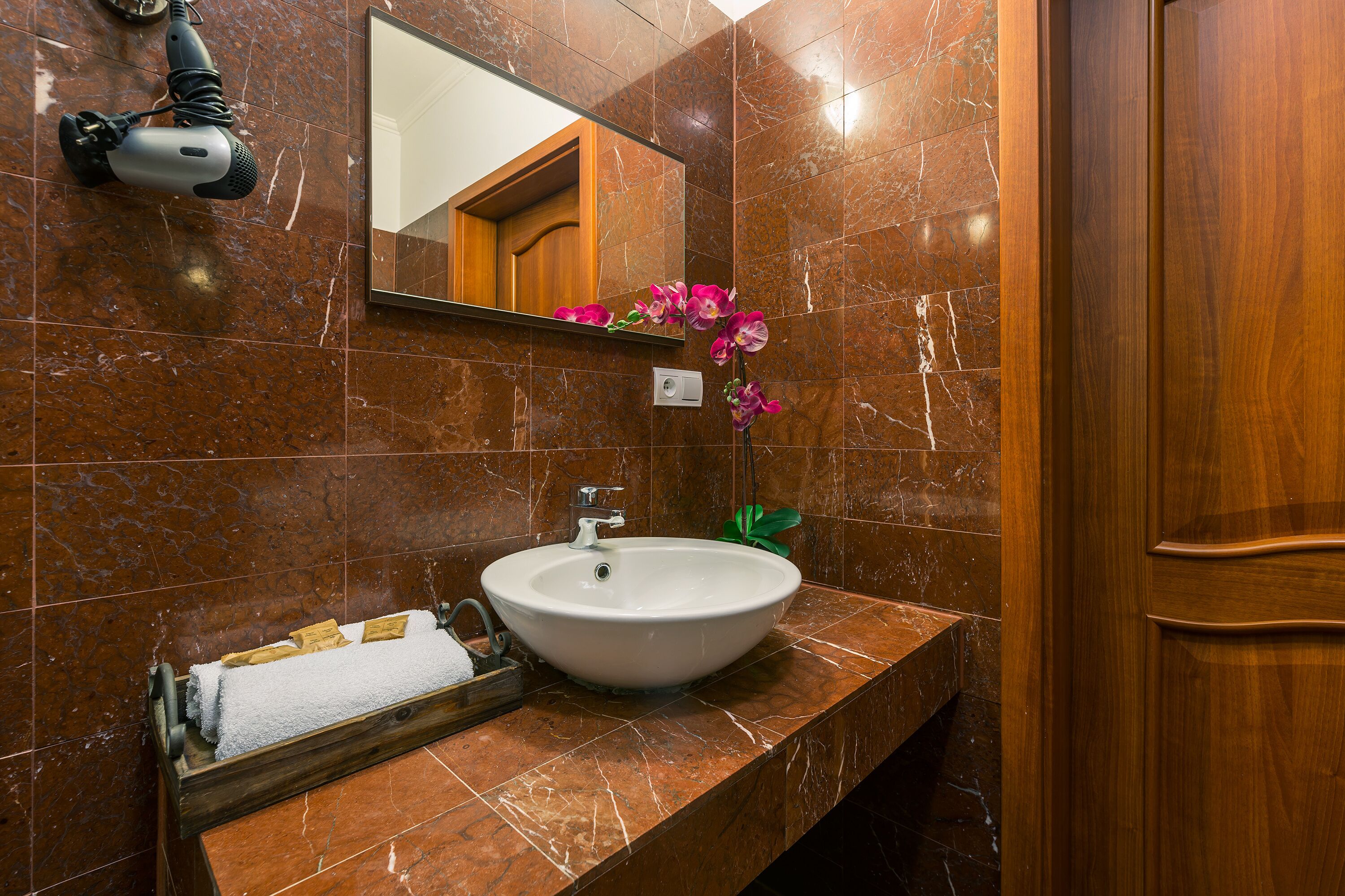 A bathroom with a marble sink, a mirror, a hairdryer, and a plant.