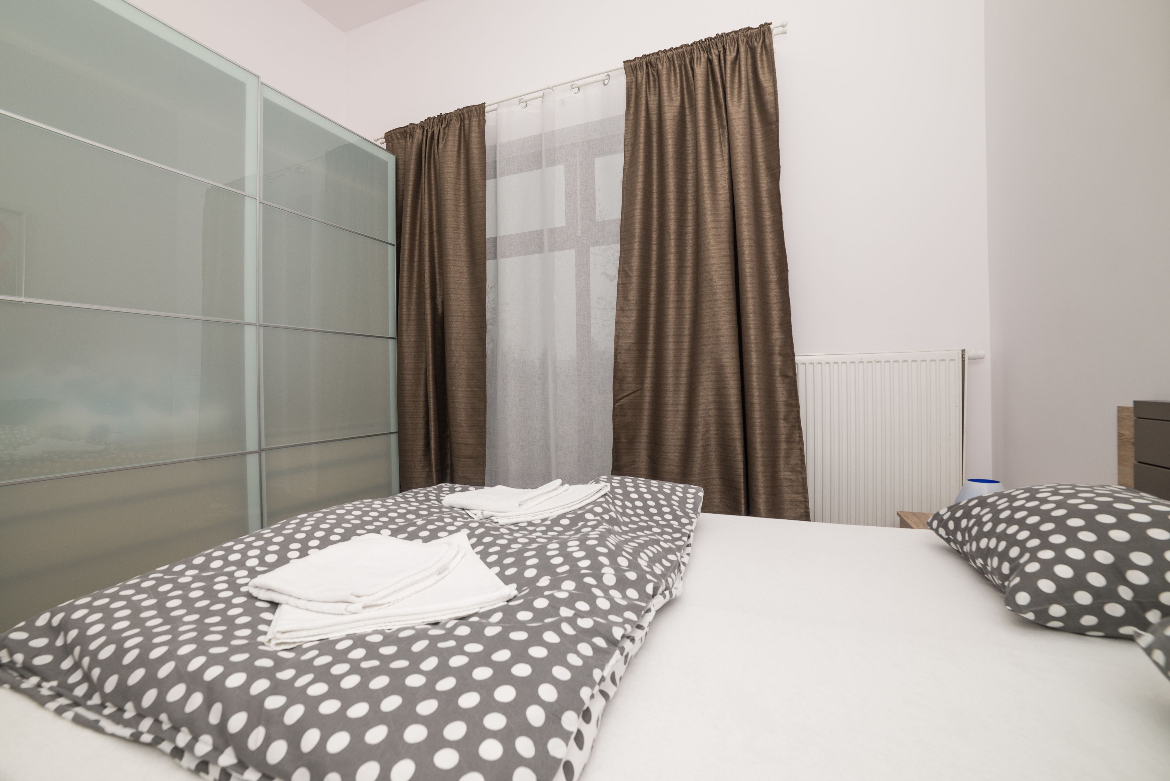 A hotel room with two beds, a large window with curtains, a radiator, and a modern design.