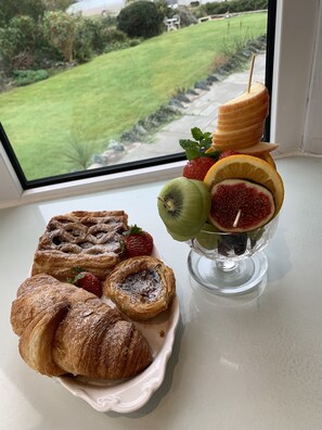 A breakfast setting with pastries and a fruit drink on a table by a window overlooking a garden. - Castellor (Cemaes Bay)