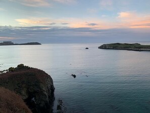 A coastal landscape with calm waters, rocky outcrops, and distant landforms. - Castellor (Cemaes Bay)