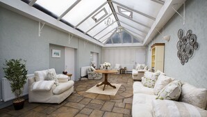 A spacious room with a high ceiling and skylights, furnished with white sofas and a central wooden table. - Castellor (Cemaes Bay)