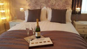 A neatly made bed with a bottle of champagne, two glasses, and a box of chocolates on the bed. - Castellor (Cemaes Bay)