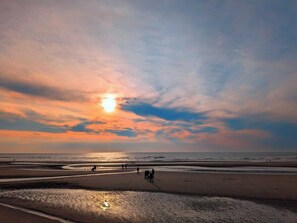 A beach scene with people walking along the shore during sunset. - San Remo Apartments Blackpool (Blackpool)