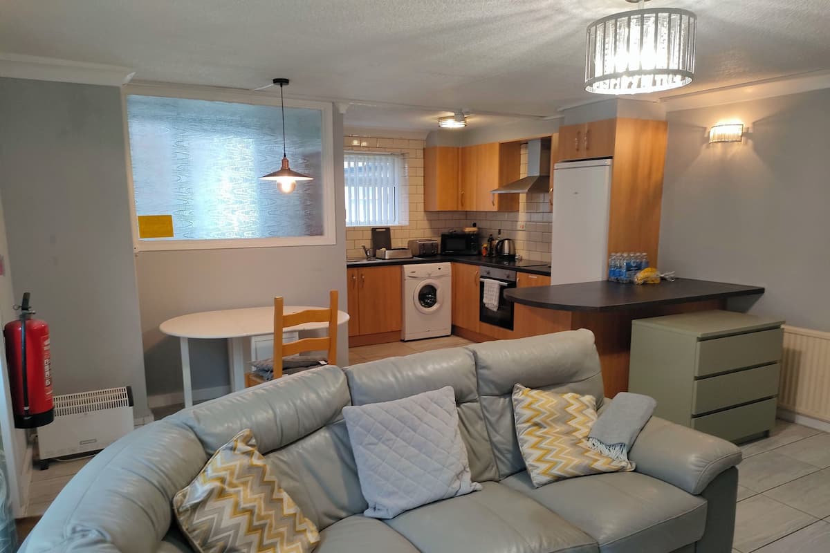 Un espace de vie compact comprenant un canapé, une petite table à manger, un lave-linge et une kitchenette.