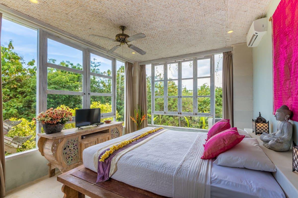 A bedroom with a large bed, a wooden desk with a TV, and a Buddha statue.