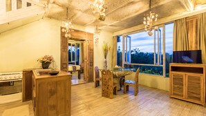 A rustic kitchen with wooden cabinets, a dining table, and a large window offering a view of the outdoors. - BoHo Bingin Beach (Pecatu)