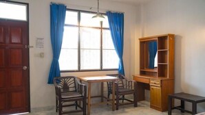 A room with a wooden desk, two chairs, a small table, a wardrobe, and a window with blue curtains. - Weekender Bungalow (Koh Samui)