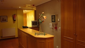 A reception area with a wooden counter, a sign labeled "RECEPTION," a fire extinguisher, a thermostat, and a wall-mounted telephone. - Hotel Campus (Burgos)