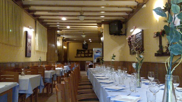 A restaurant with long tables set for dining, wooden chairs, and a TV mounted on the wall. - Hotel Campus (Burgos)