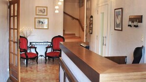 Un pasillo con un mostrador de recepción de madera, sillas rojas y una escalera al fondo.