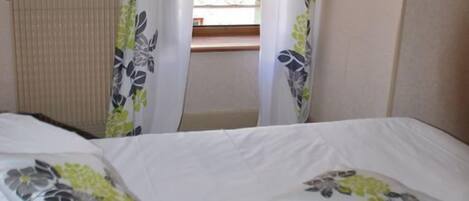Habitación de hotel con cama, cortinas florales y ventana con vista a un balcón.