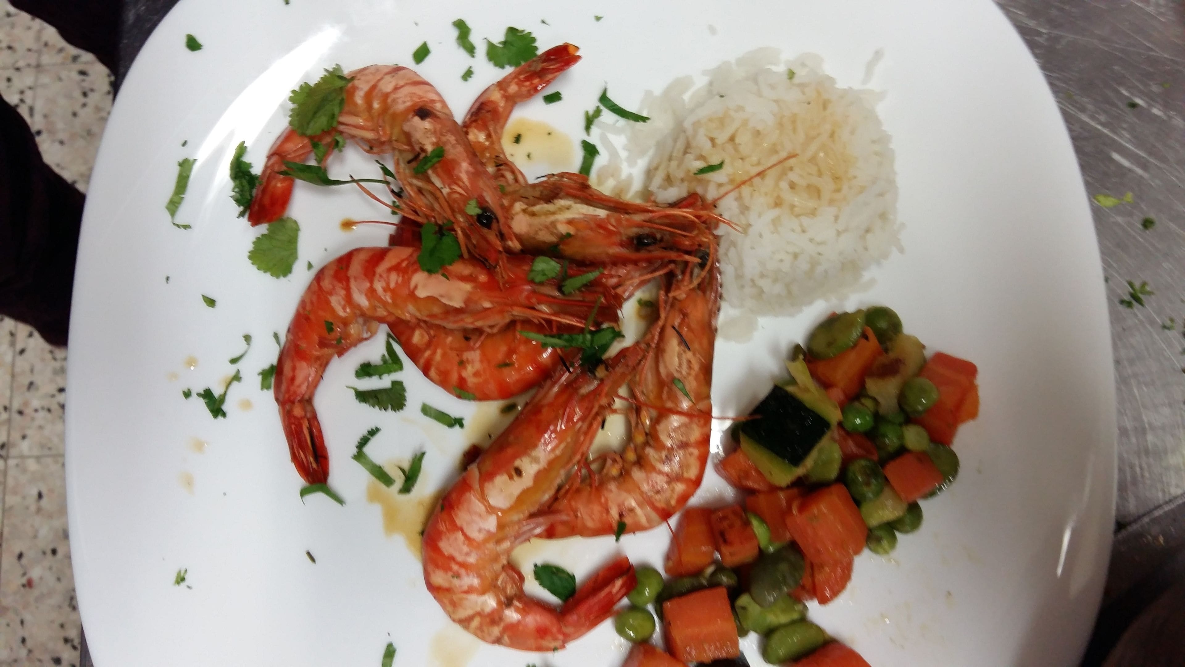 Une assiette contenant des crevettes cuites, du riz et un mélange de légumes.