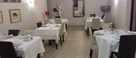 A dining area with tables set for service, a mirror on the wall, and a white decorative piece on the wall.