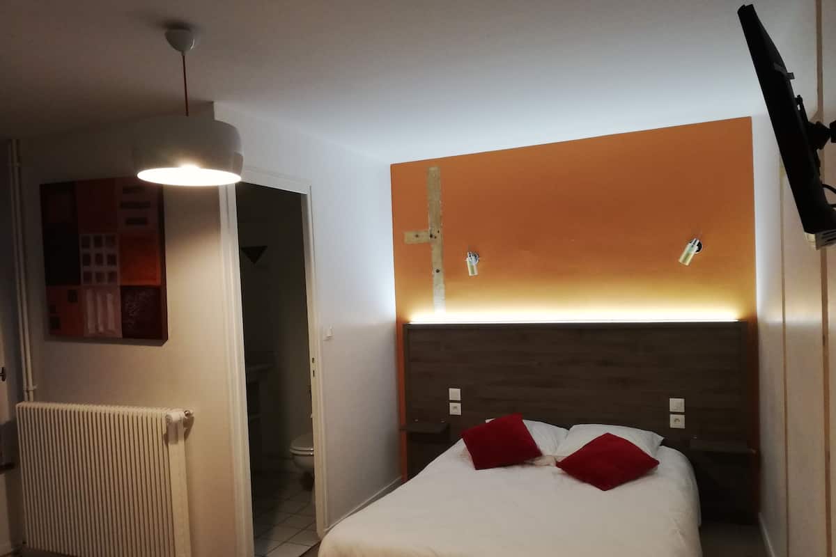 A hotel room with a bed, a radiator, a door leading to a bathroom, and a wall-mounted TV.