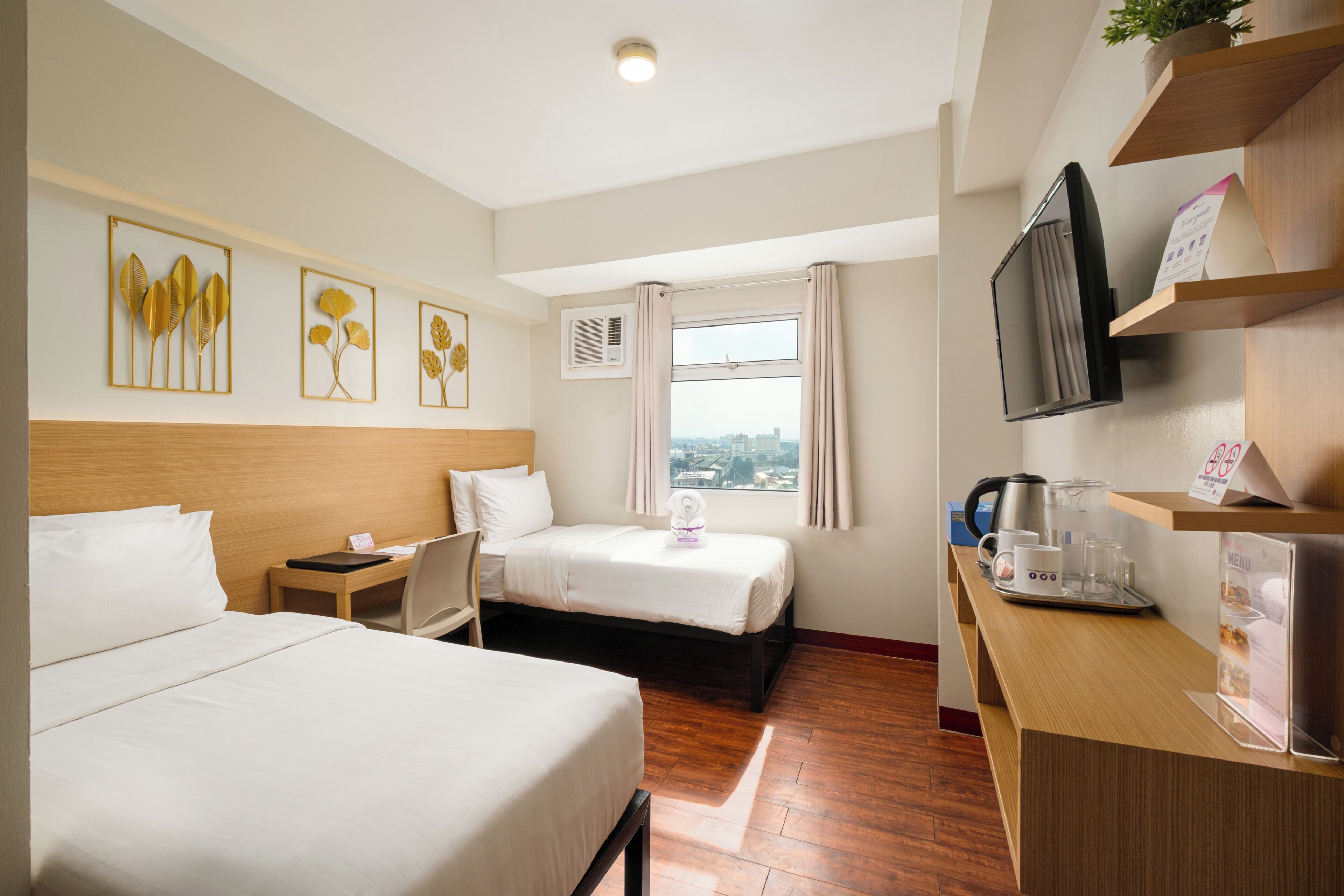 Habitación de hotel con dos camas, un escritorio con cafetera, televisión y obras de arte en la pared.