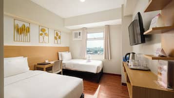 Habitación de hotel con dos camas, un escritorio con cafetera, televisión y obras de arte en la pared.