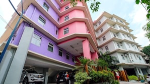 A multi-story residential building with a purple and pink facade, a covered parking area, and a person standing near the entrance. - MySpace Hotel at BGC (Taguig)