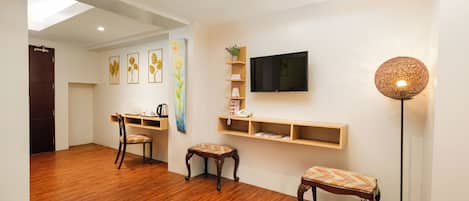 Une pièce avec un plancher en bois, un bureau avec une chaise, un téléviseur fixé au mur et un lampadaire.