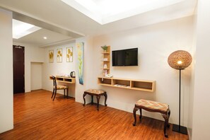 Une pièce avec un plancher en bois, un bureau avec une chaise, un téléviseur fixé au mur et un lampadaire.