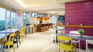 A modern dining area with yellow chairs, a wooden counter, and a pink accent wall. - MySpace Hotel at BGC (Taguig)