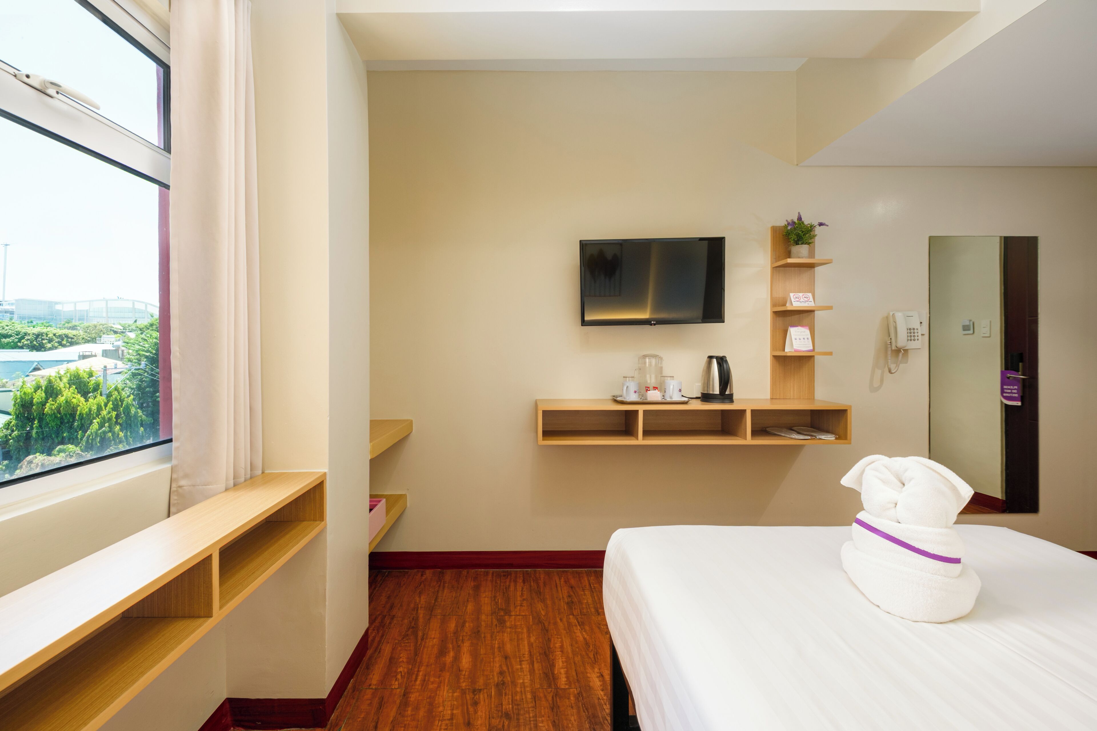 A hotel room with a bed, a TV, a coffee maker, and a window with a view of greenery.