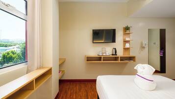 Hotelkamer met een bed, televisie, koffiezetapparaat en raam met uitzicht op groen.