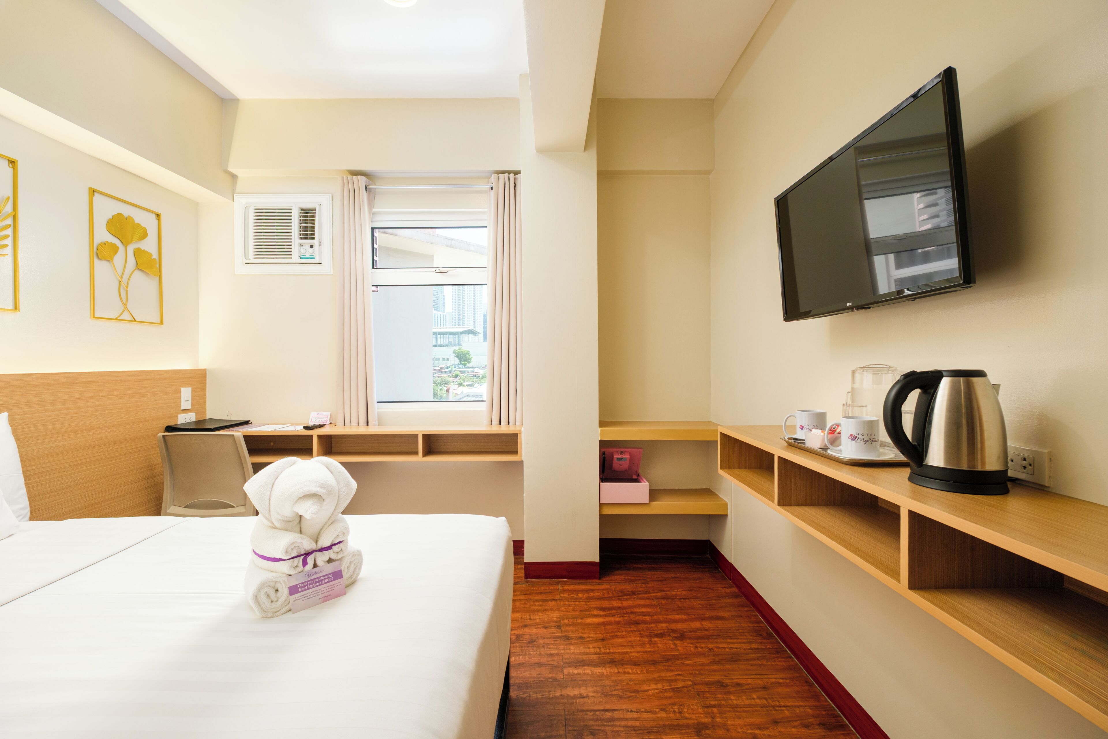 Una habitación de hotel con cama, escritorio, televisión, ventana con cortinas y cafetera.