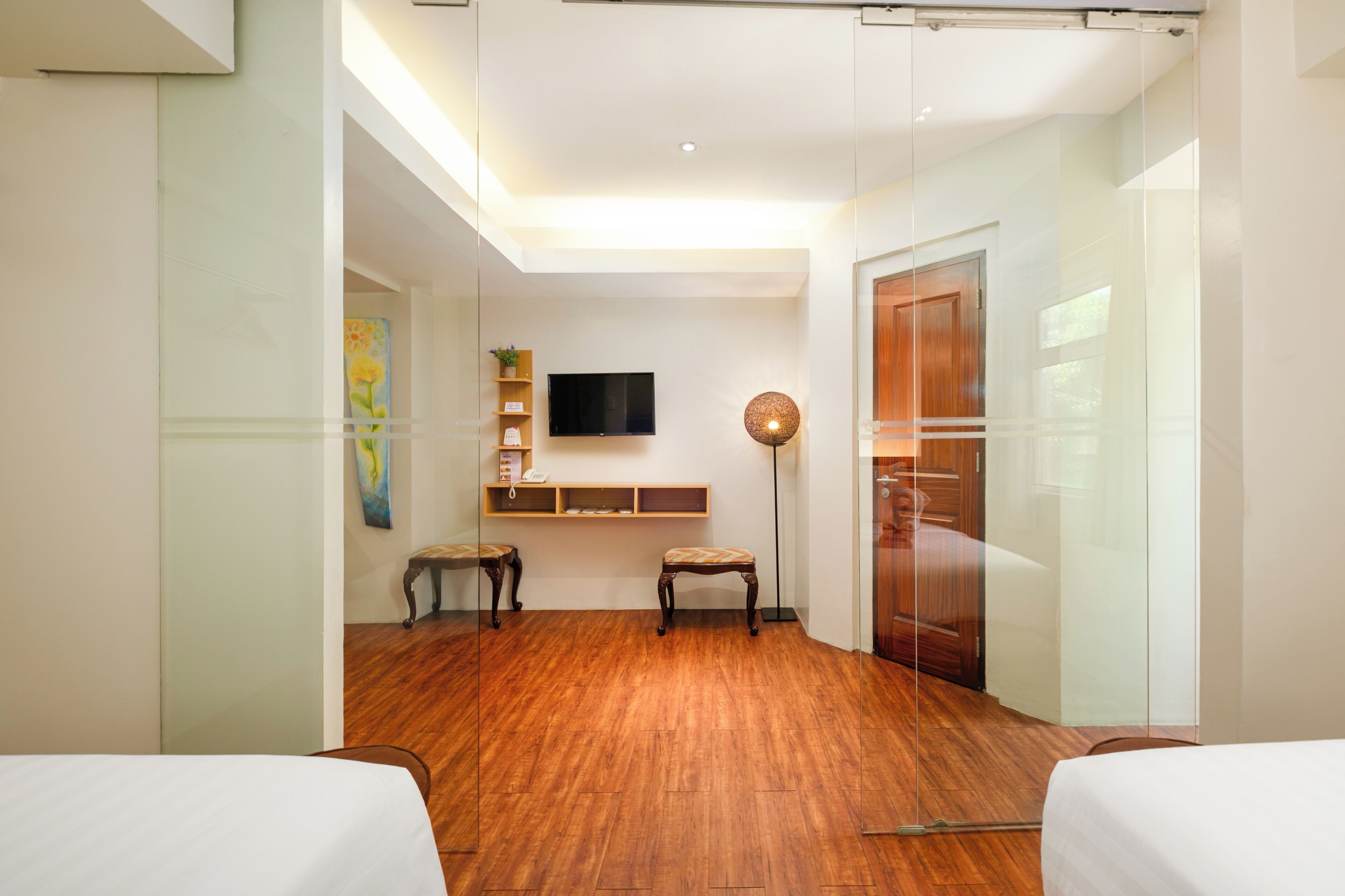 A modern hotel room with a wooden floor, a flat-screen TV, a small table with chairs, a painting on the wall, and a sliding door.
