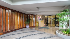A modern lobby with a wooden panel wall, a reception desk, and a potted plant. - MySpace Hotel at BGC (Taguig)