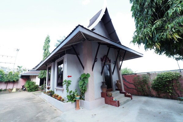 A small, single-story building with a sloped roof, a porch with steps, and a garden area with potted plants and a small statue. - Sweet Inn Resort Hotel (Bang Pahan)