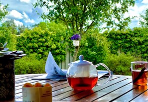 A wooden table with a teapot, a cup of tea, a basket of oranges, and a book. - Sarpsborg Apartments (Sarpsborg)