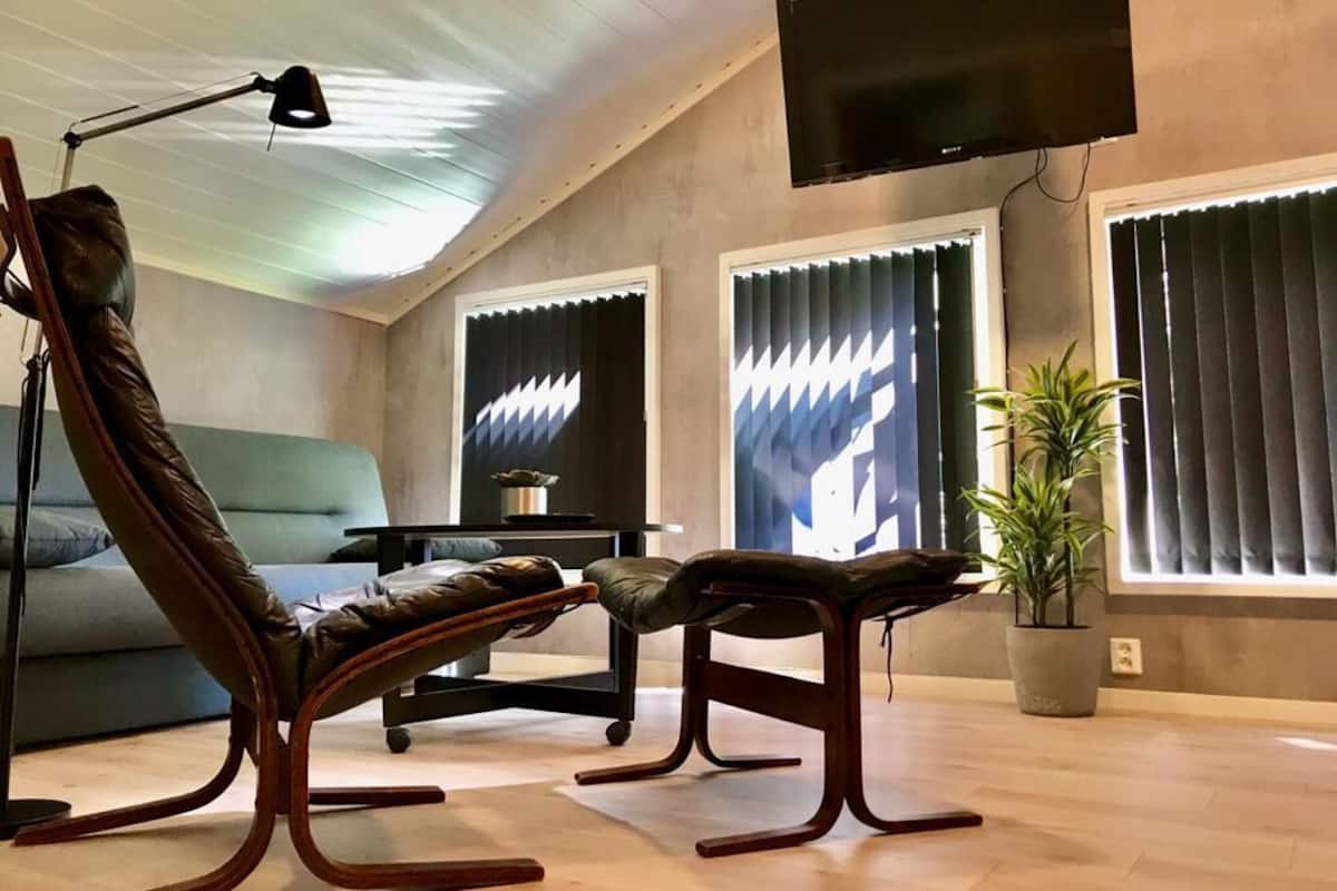 Una sala de estar moderna con un sofá, dos sillones, un televisor y una planta en maceta.