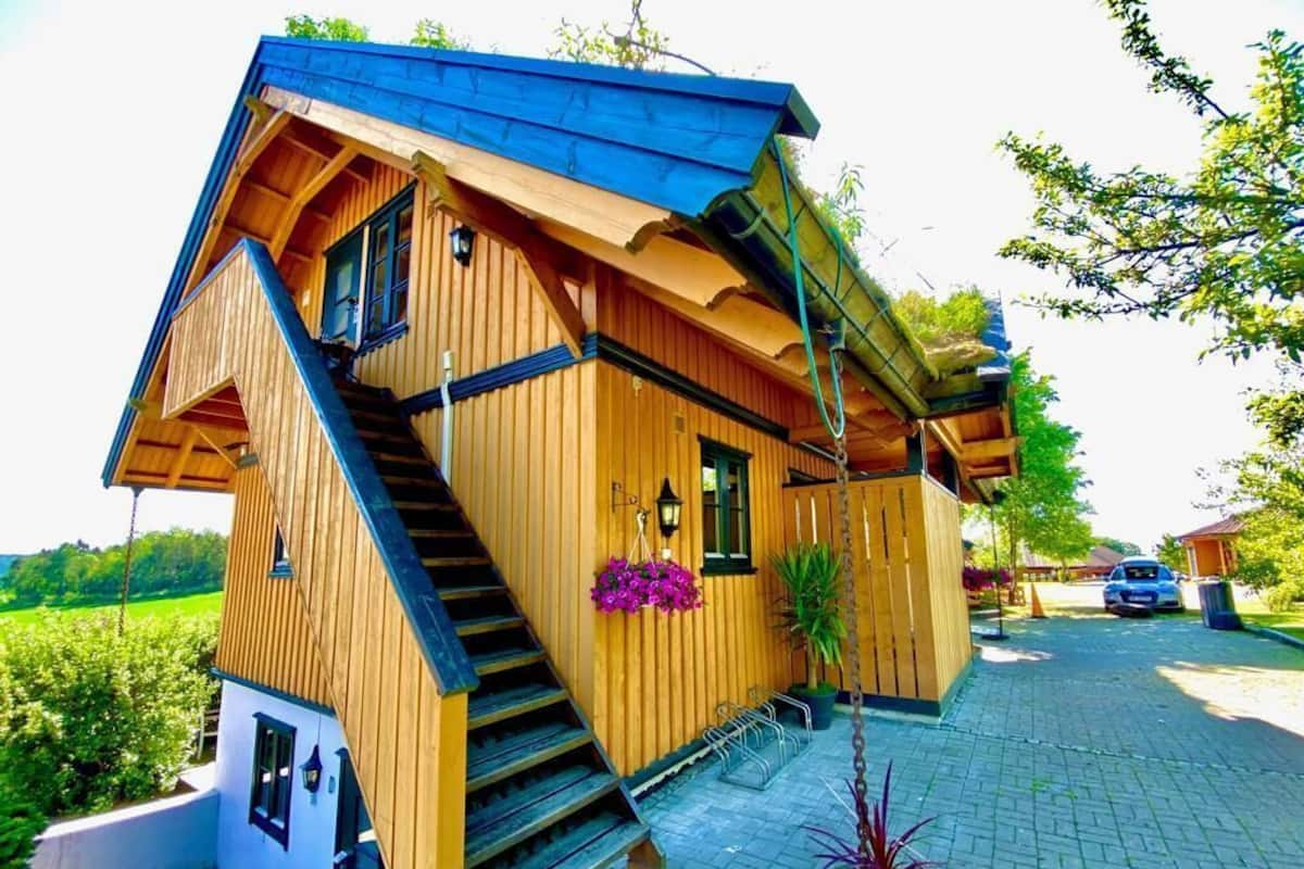 Una casa de madera con techo inclinado, un porche delantero y una escalera que lleva a la entrada.