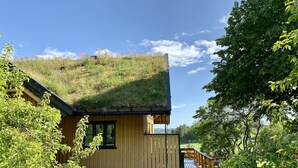 Une cabane en bois avec un toit de chaume, une terrasse en bois et un chemin pavé menant à l’entrée.