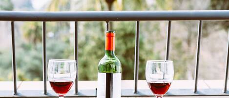 Una mesa con una botella y dos copas de vino tinto en un balcón con vistas a palmeras.