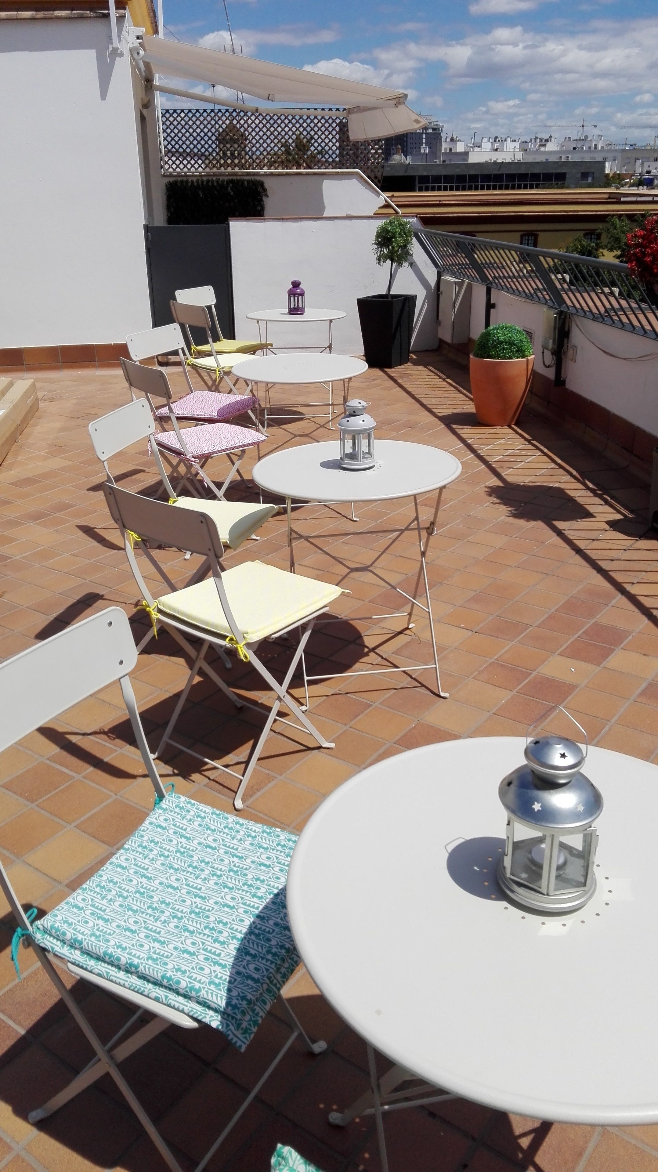 A rooftop terrace with white folding chairs, a round table, and a potted plant.