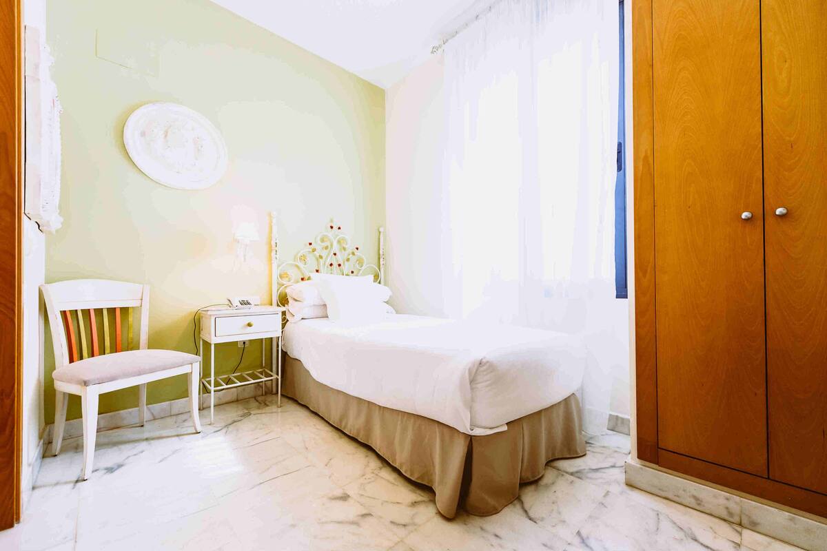 A bedroom with a bed, a bedside table, a chair, and a wardrobe.