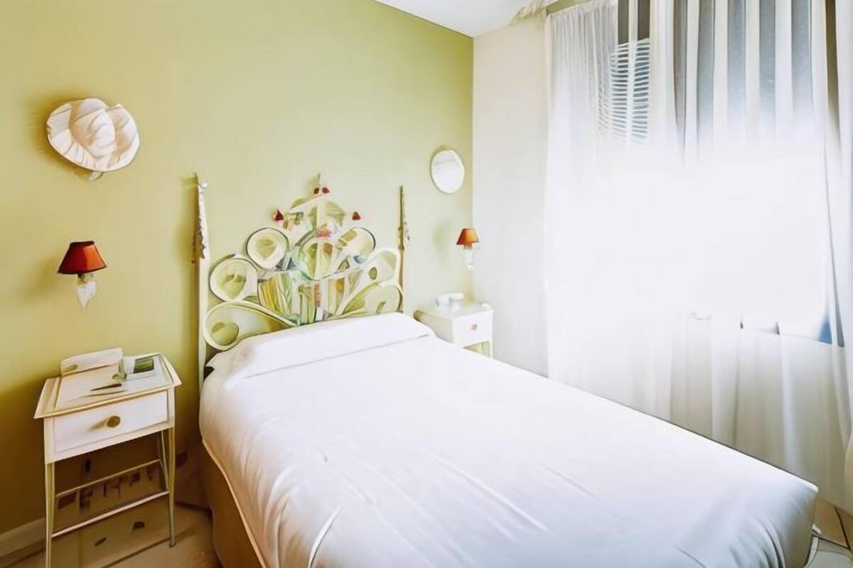 A bedroom with a bed, bedside table, lamp, and curtains.