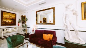 A lobby with a green velvet sofa, a marble coffee table, a large painting, a statue, and a mirror with a gold frame. - Basic Hotel Doña Manuela (Seville)