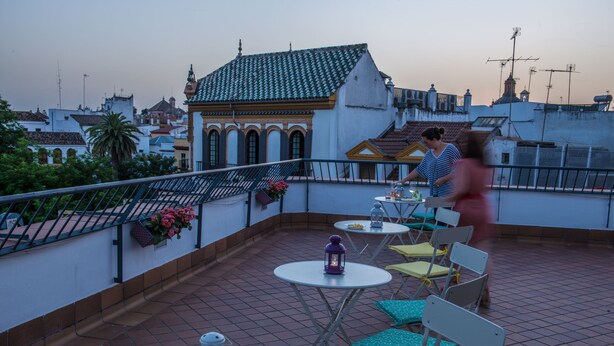 A rooftop terrace with tables and chairs, a lantern, and a view of the cityscape. - Basic Hotel Doña Manuela (Seville)