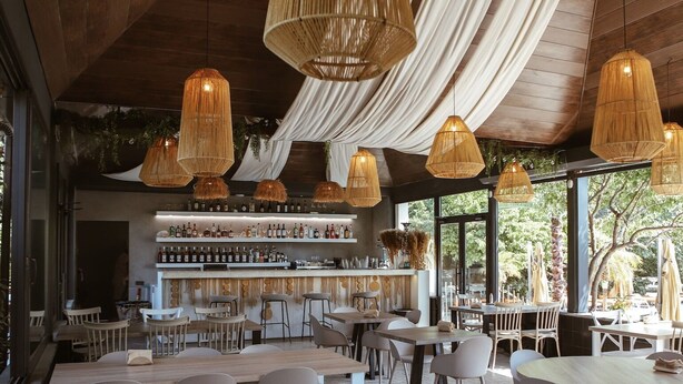 A restaurant with wooden tables and chairs, hanging wicker lamps, and a bar area with shelves of bottles. - Cross Resort Yerevan (Yerevan)