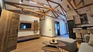 A modern living room with exposed wooden beams, a flat-screen TV, and a cozy seating area. - Cross Resort Yerevan (Yerevan)