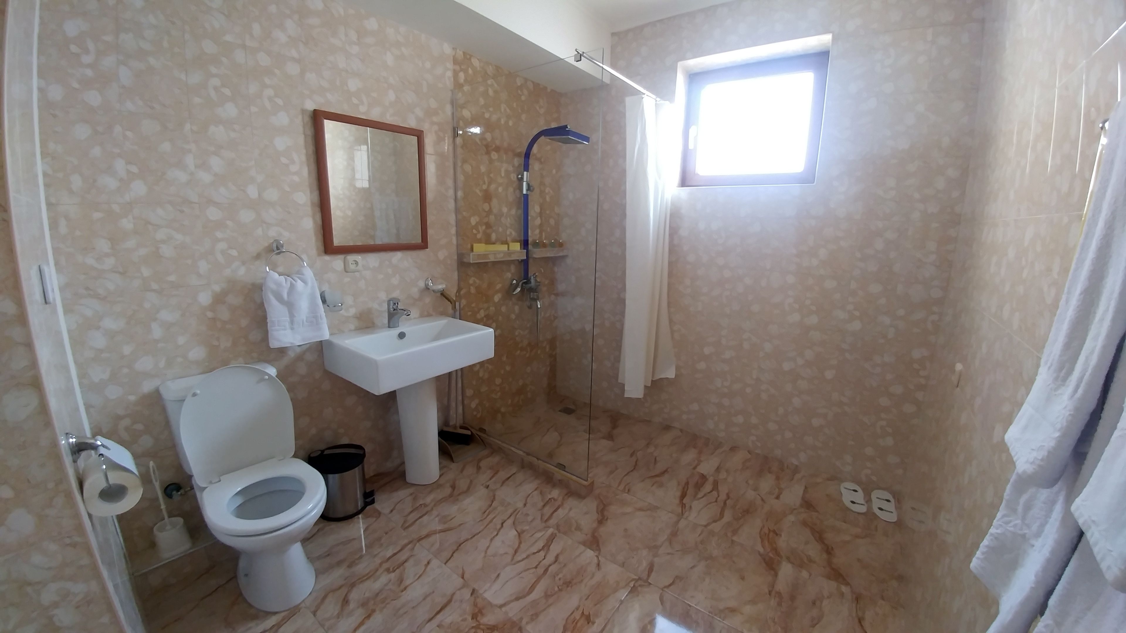 Een badkamer met toilet, wastafel, douche en een klein raam.