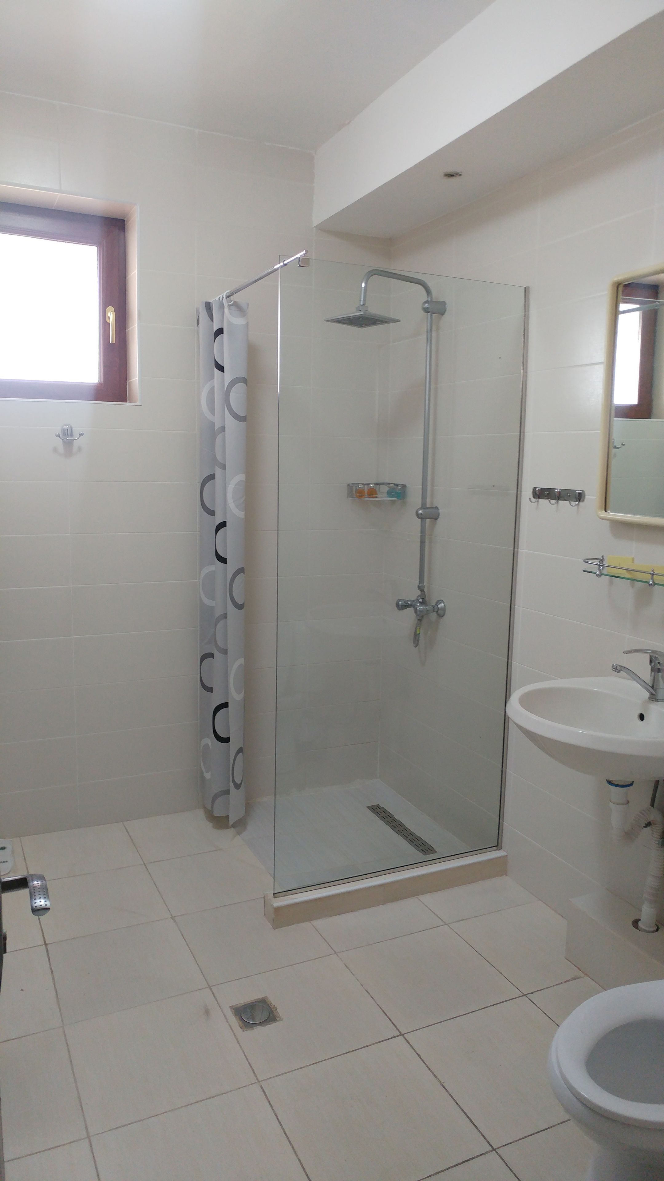 A bathroom with a glass-enclosed shower, a sink, and a window.