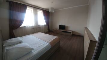 Un dormitorio con cama, cortinas, un televisor sobre un mueble de madera y una lámpara colgante.