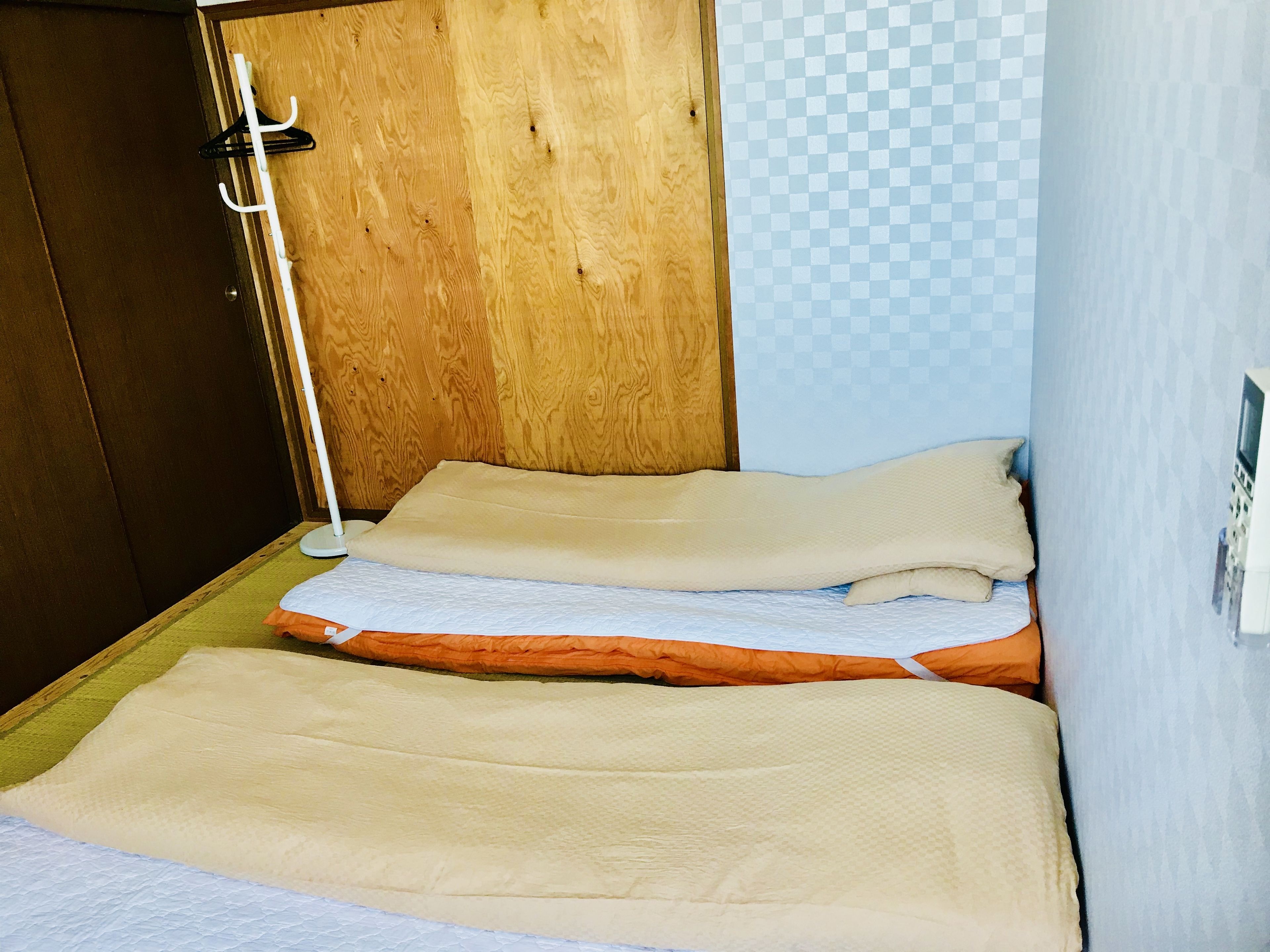 A small, compact room with two beds, a wooden door, and a checkered wall.