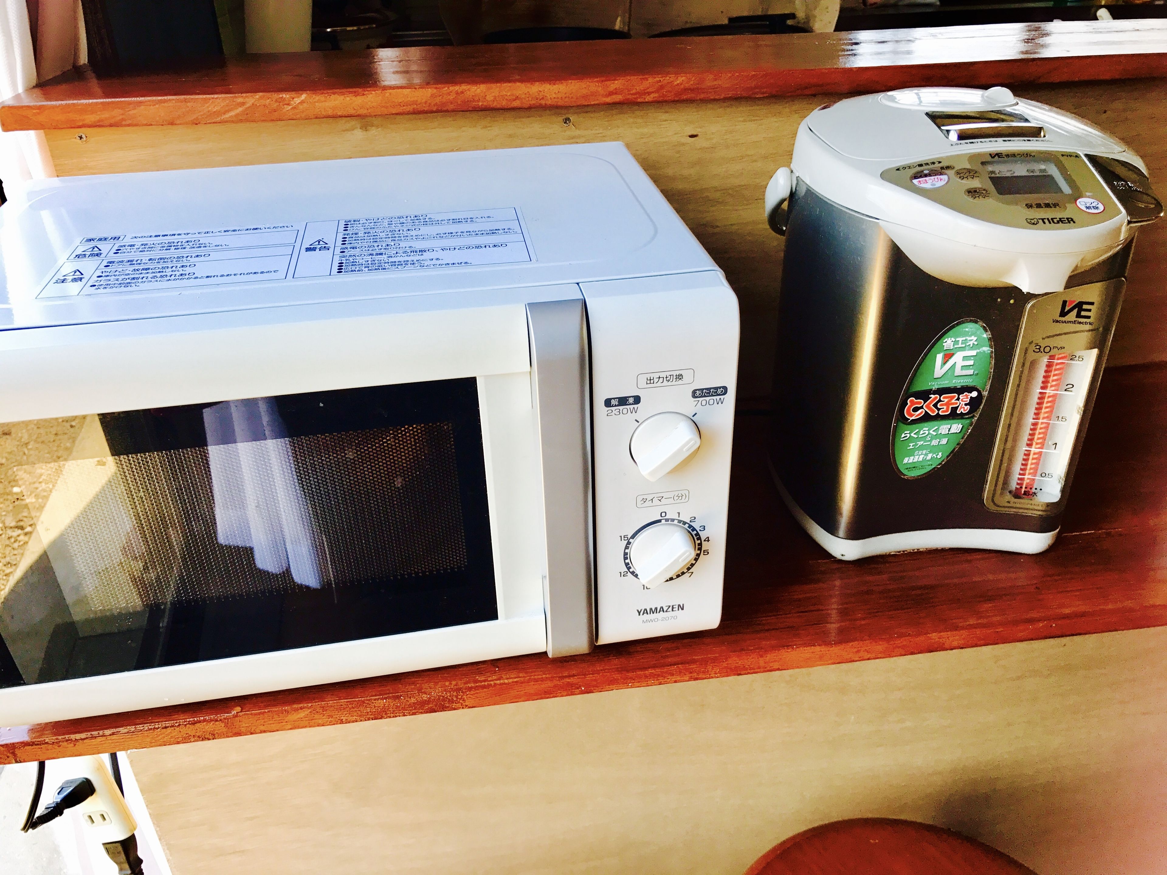 A microwave and a rice cooker on a wooden countertop.