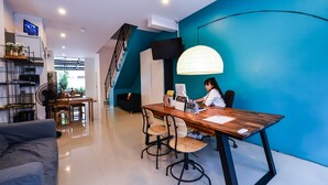 A modern living room with a teal accent wall, a wooden dining table, and a person working at a desk. - Two Color Patong (Patong)